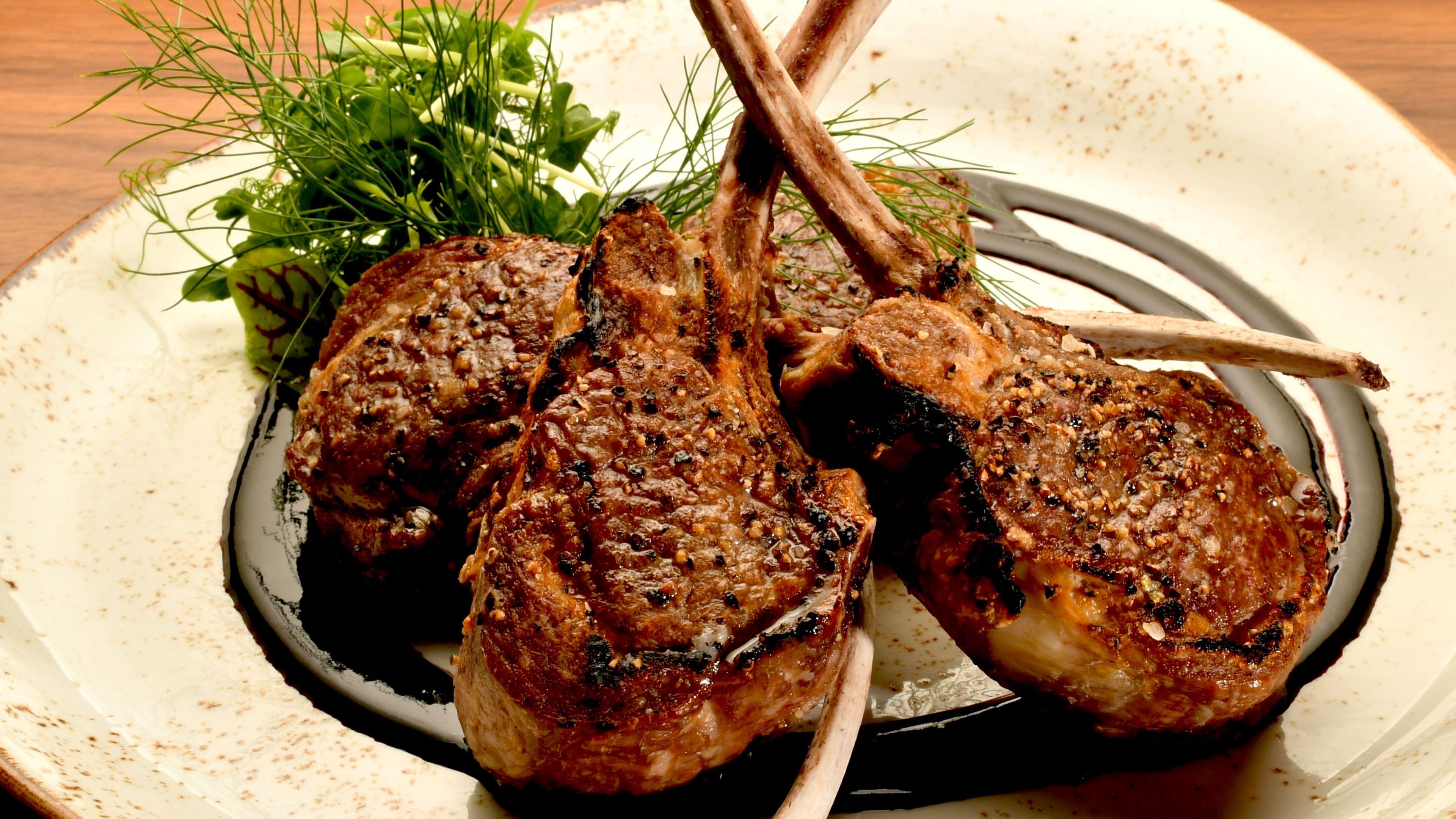 A plate with two grilled lamb chops, a side of greens, and a decorative element.