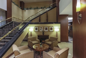 Un hall d’entrée avec une cheminée, deux fauteuils, une table basse et un escalier.