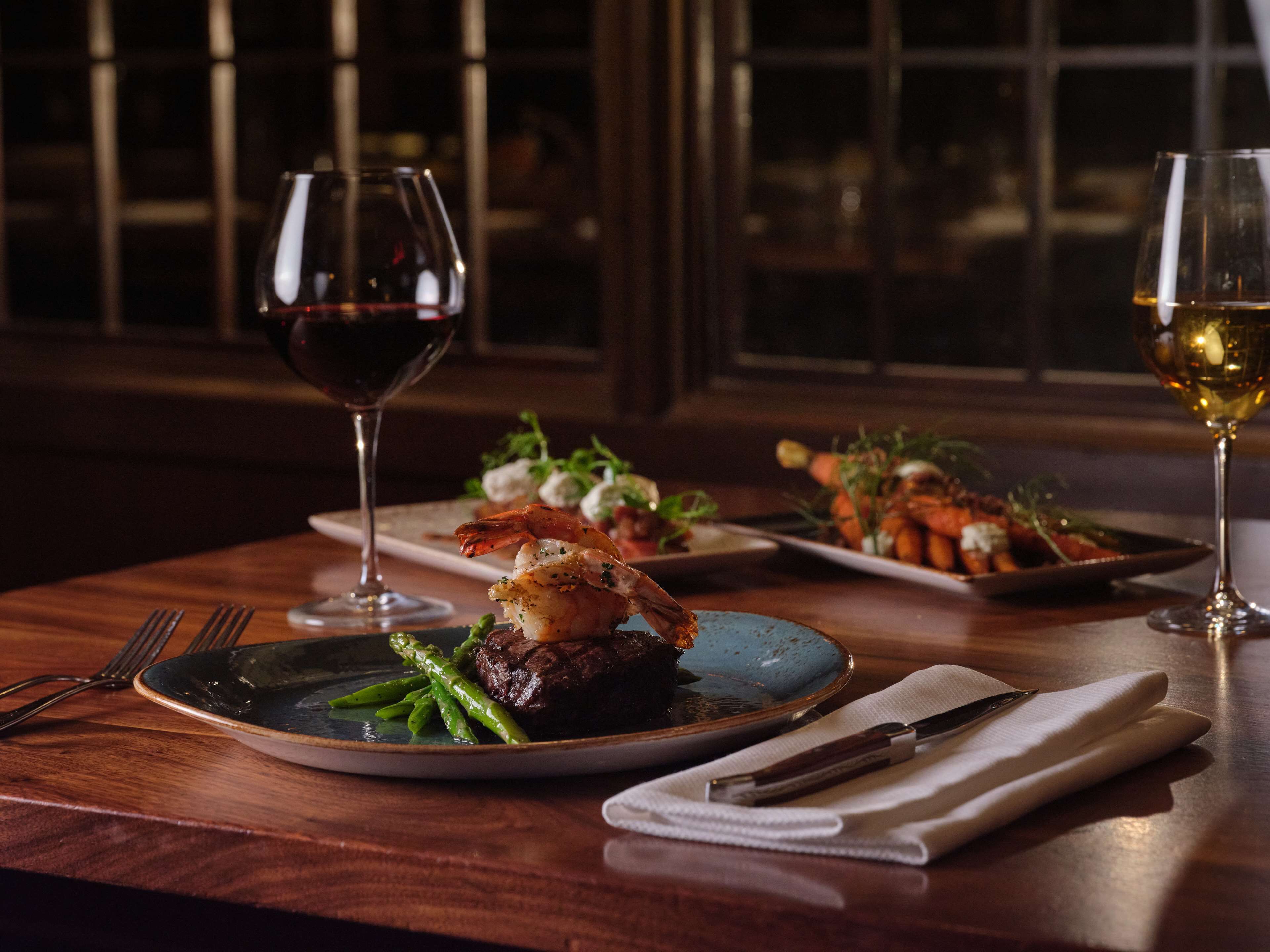 A dining table with plates of food, wine glasses, and cutlery.