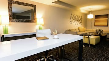 Une chambre d’hôtel avec un bureau blanc, deux lampes, un canapé, une table basse et un élément décoratif mural.