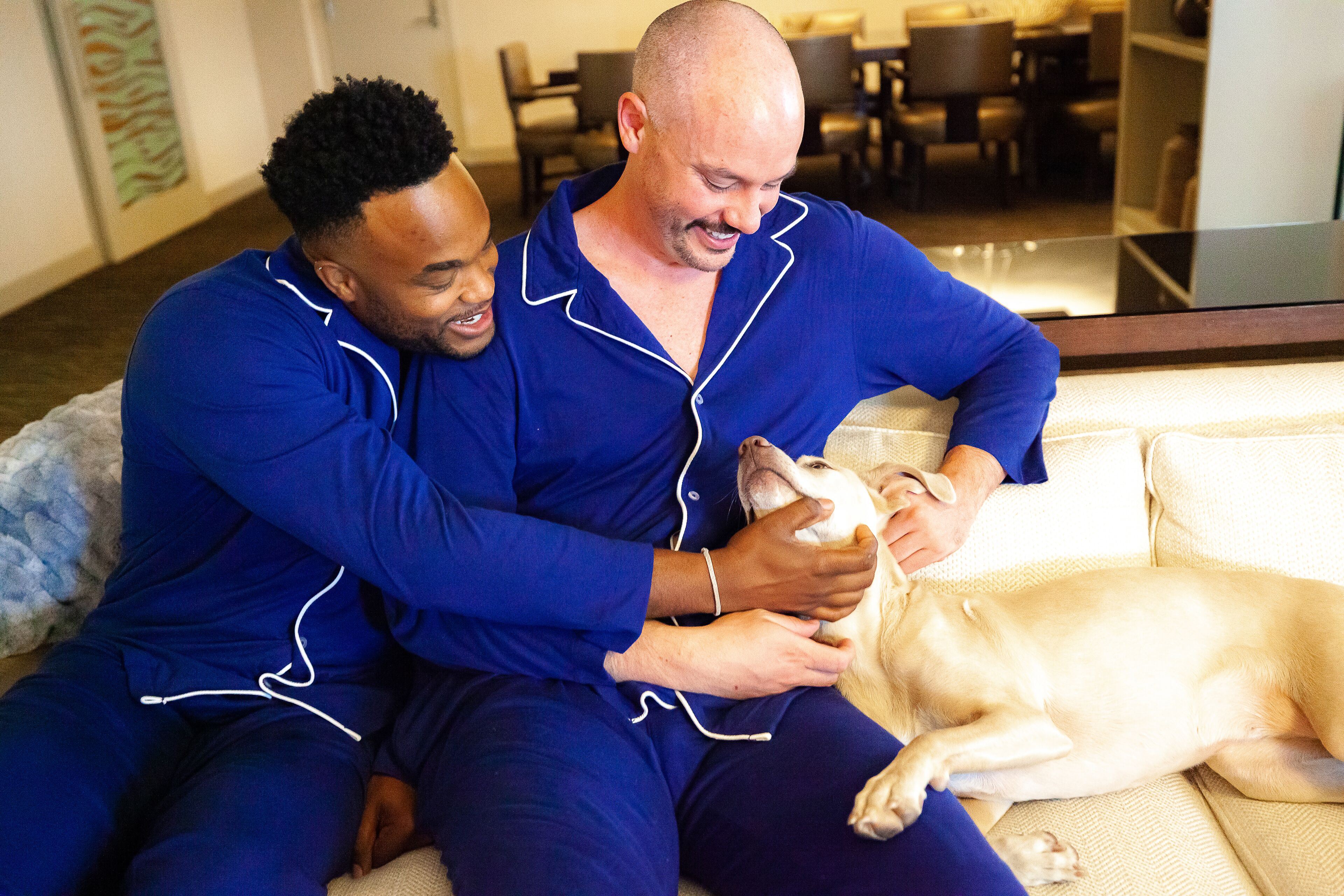 Dos personas en pijamas azules sentadas en un sofá con un perro.