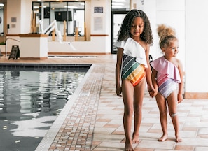 Deux enfants se promènent près d’une piscine dont le sol est recouvert de carreaux, et on aperçoit l’intérieur du bâtiment.