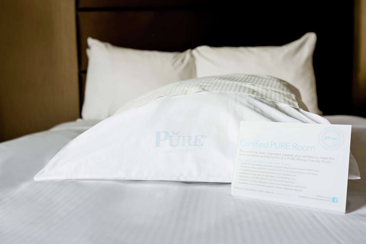 Un lit avec une literie blanche et un panneau indiquant qu’il s’agit d’une chambre certifiée « Pure Room ».