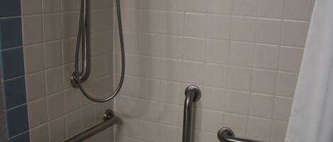 A bathroom with a bathtub, grab bars, and a shower head.