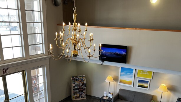 Een ruime woonkamer met een kroonluchter, een bank, een salontafel en een aan de muur bevestigde televisie.