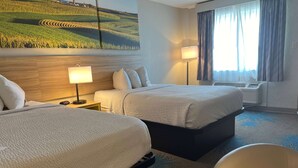 Een hotelkamer met twee bedden, een nachtkastje, een lamp, een stoel en een groot schilderij aan de muur.