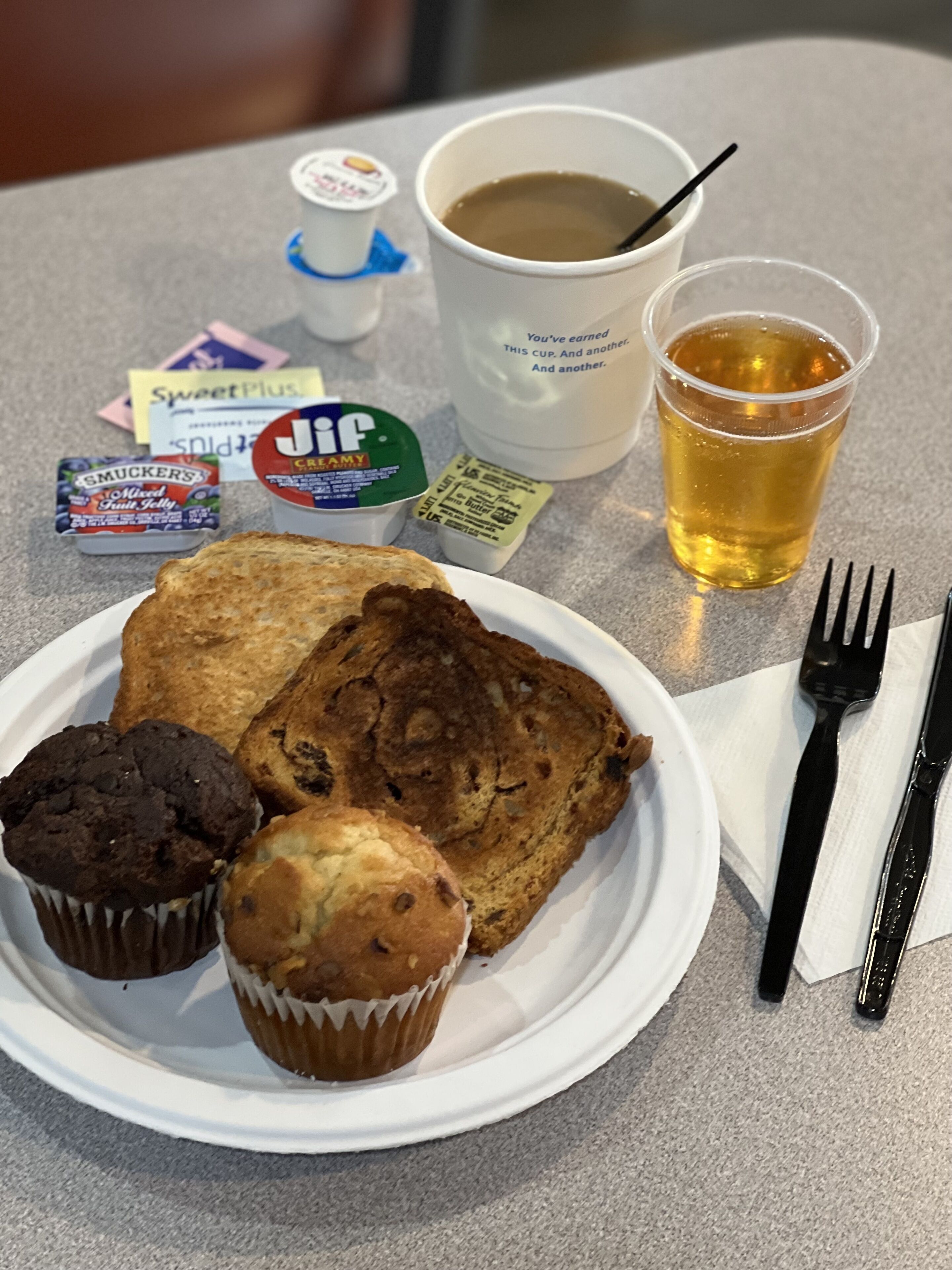A plate with muffins and a scone, a cup of tea, and a plastic cup with a beverage.