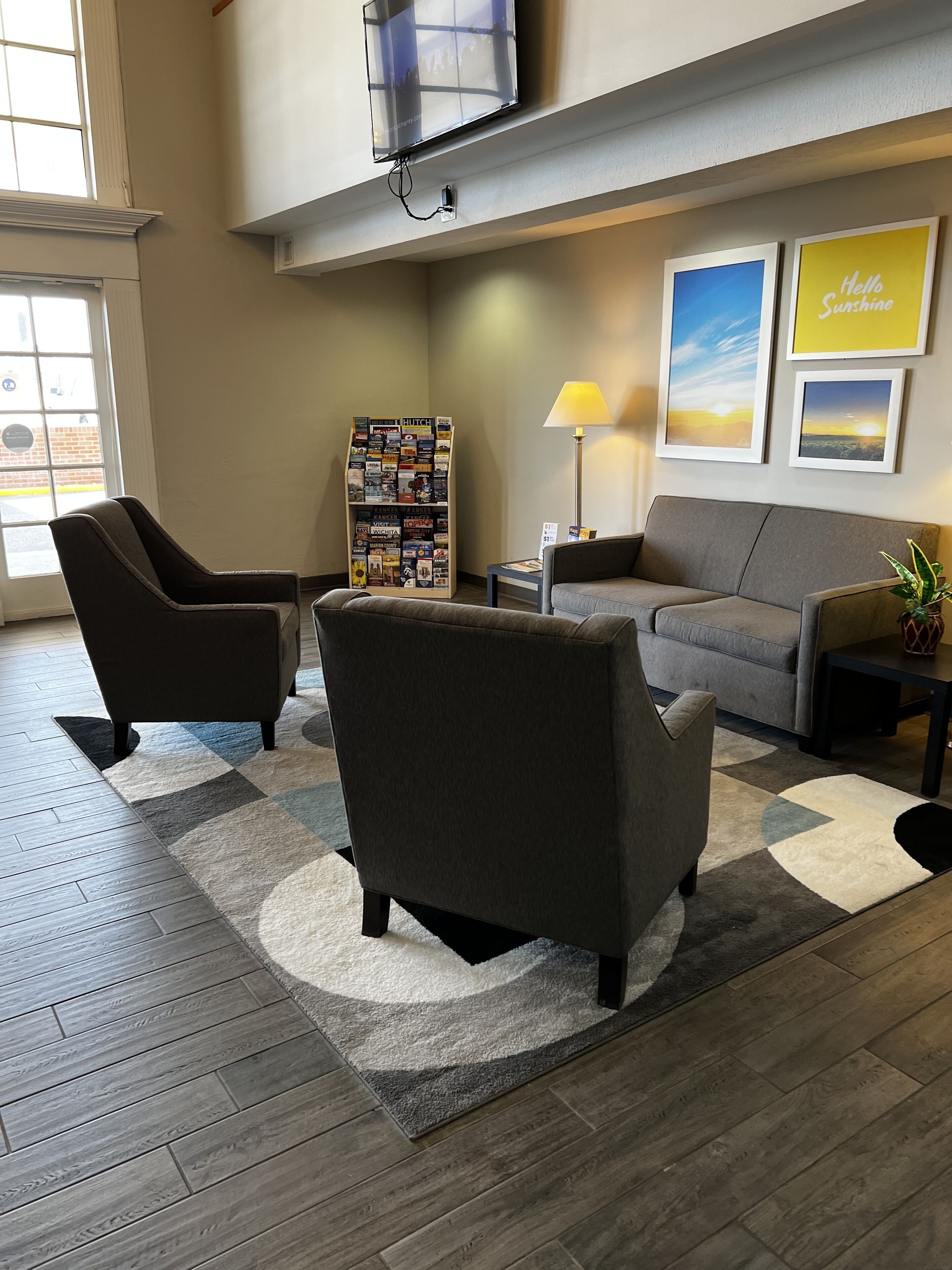 A modern lobby with a grey sofa, two armchairs, a coffee table, a bookshelf, and a TV mounted on the wall.