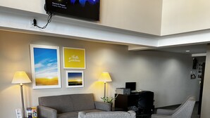 Een moderne lobby met een grijze bank, twee fauteuils, een flatscreen-tv en kunstwerken in lijsten.