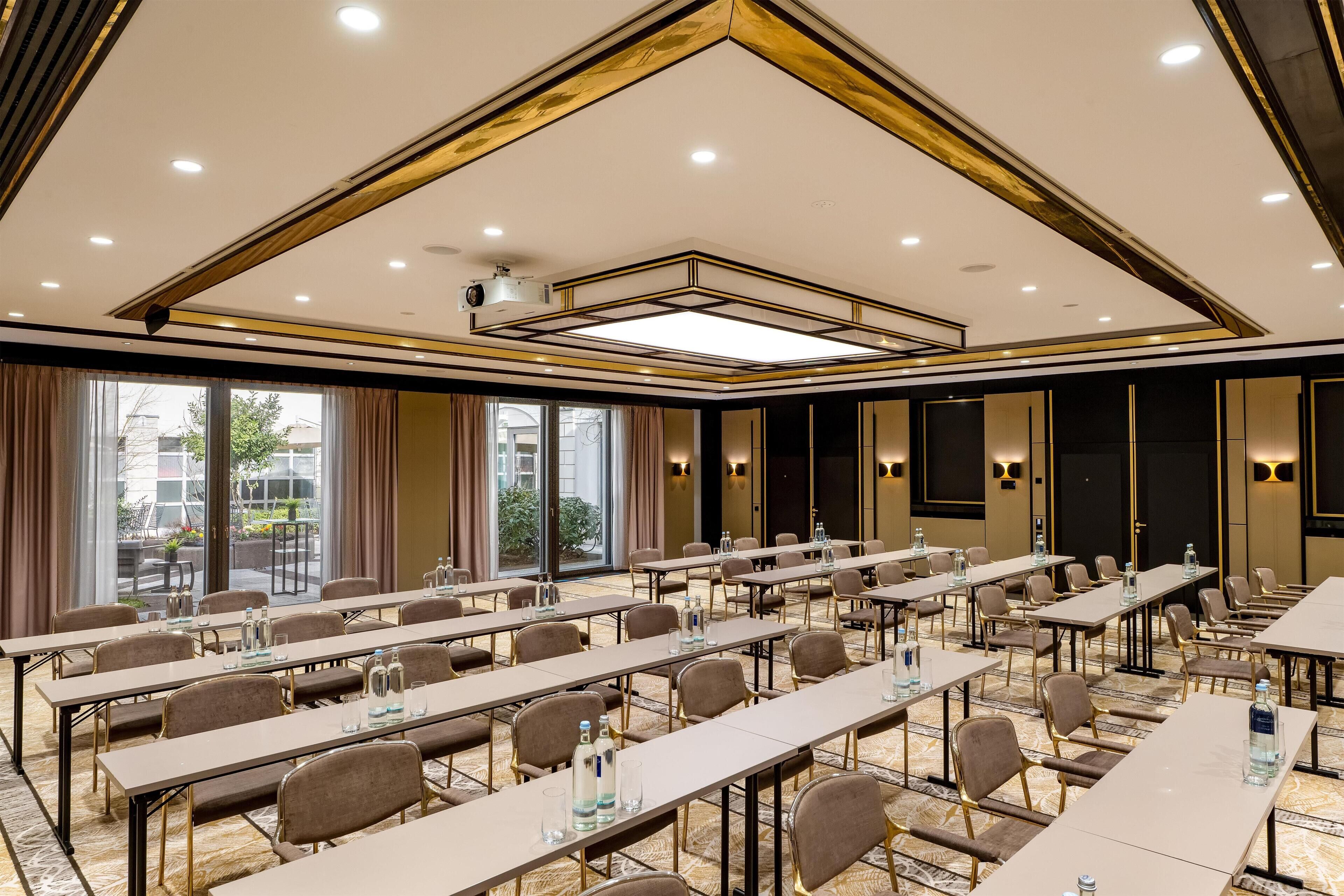 A conference room with long tables, chairs, and a ceiling with recessed lighting and a central light fixture.
