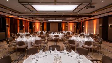 Un salón de banquetes con varias mesas redondas dispuestas para comer, equipado con manteles blancos, sillas y cubertería.