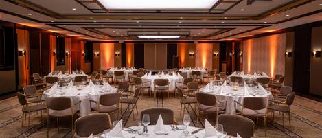 A banquet hall with multiple round tables set for dining, equipped with white tablecloths, chairs, and glassware.