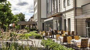 An outdoor dining area with tables and chairs, a sign for Steigenberger, and a well-maintained garden. - Steigenberger Hotel Bad Homburg (Bad Homburg v.d. Hoehe)