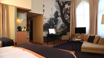 Habitación de hotel con una cama grande, un sofá, un escritorio con una silla, un televisor y un mural en la pared.