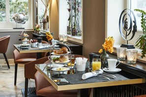 Ein Frühstückstisch mit einer Etage voller Gebäck, einer Kaffeetasse und einem Strauß gelber Blumen.