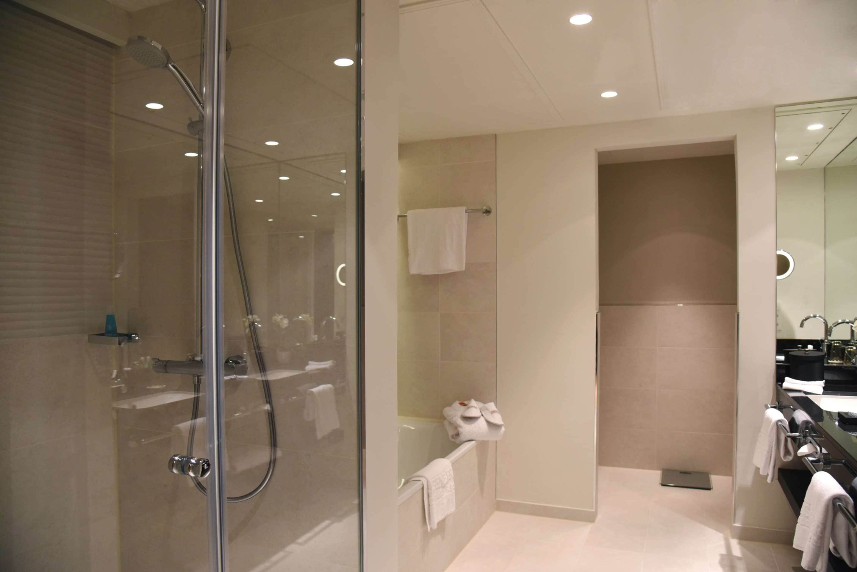 Een moderne badkamer met een glazen douchecabine, een badkuip en een wastafel met spiegel.