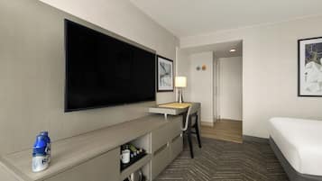 Une chambre d’hôtel équipée d’un téléviseur à écran plat, d’un bureau avec une lampe, d’un lit et d’un mini-bar.
