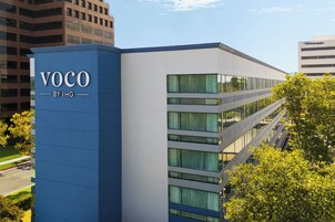 Um edifício moderno com fachada azul e branca marcante, exibindo o nome 'VOCO BY IHG' na lateral.