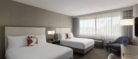 A hotel room with two beds, a desk, a chair, and a large window with curtains.