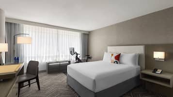 A hotel room with a large bed, a desk, a chair, a bicycle, and a phone on the nightstand.