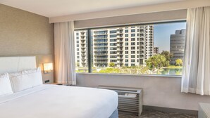 A hotel room with a large bed, a view of high-rise buildings, and a window with curtains. - voco Orange County - Airport by IHG (Santa Ana)