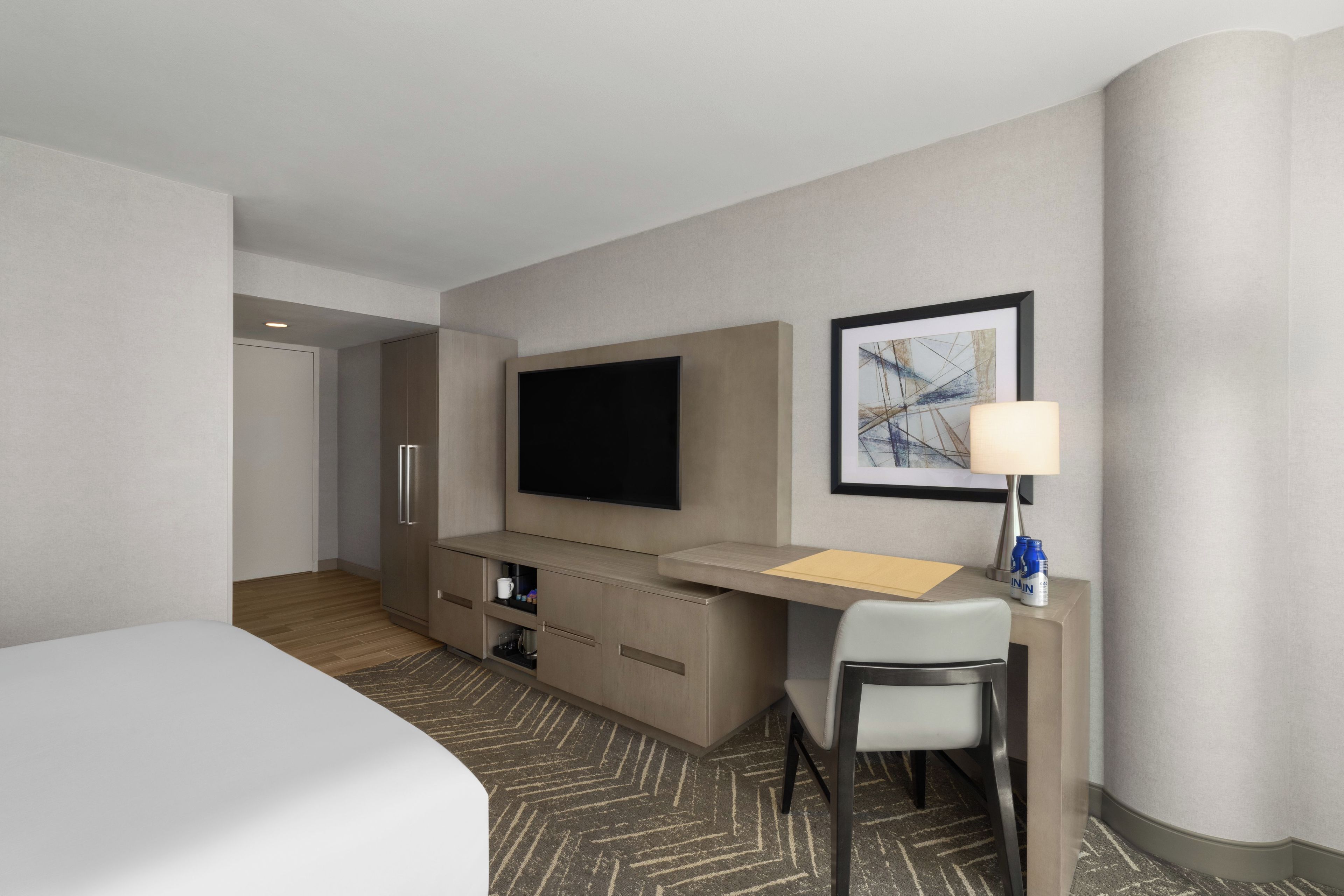 A hotel room with a bed, a desk, a chair, a television, and a framed picture on the wall.