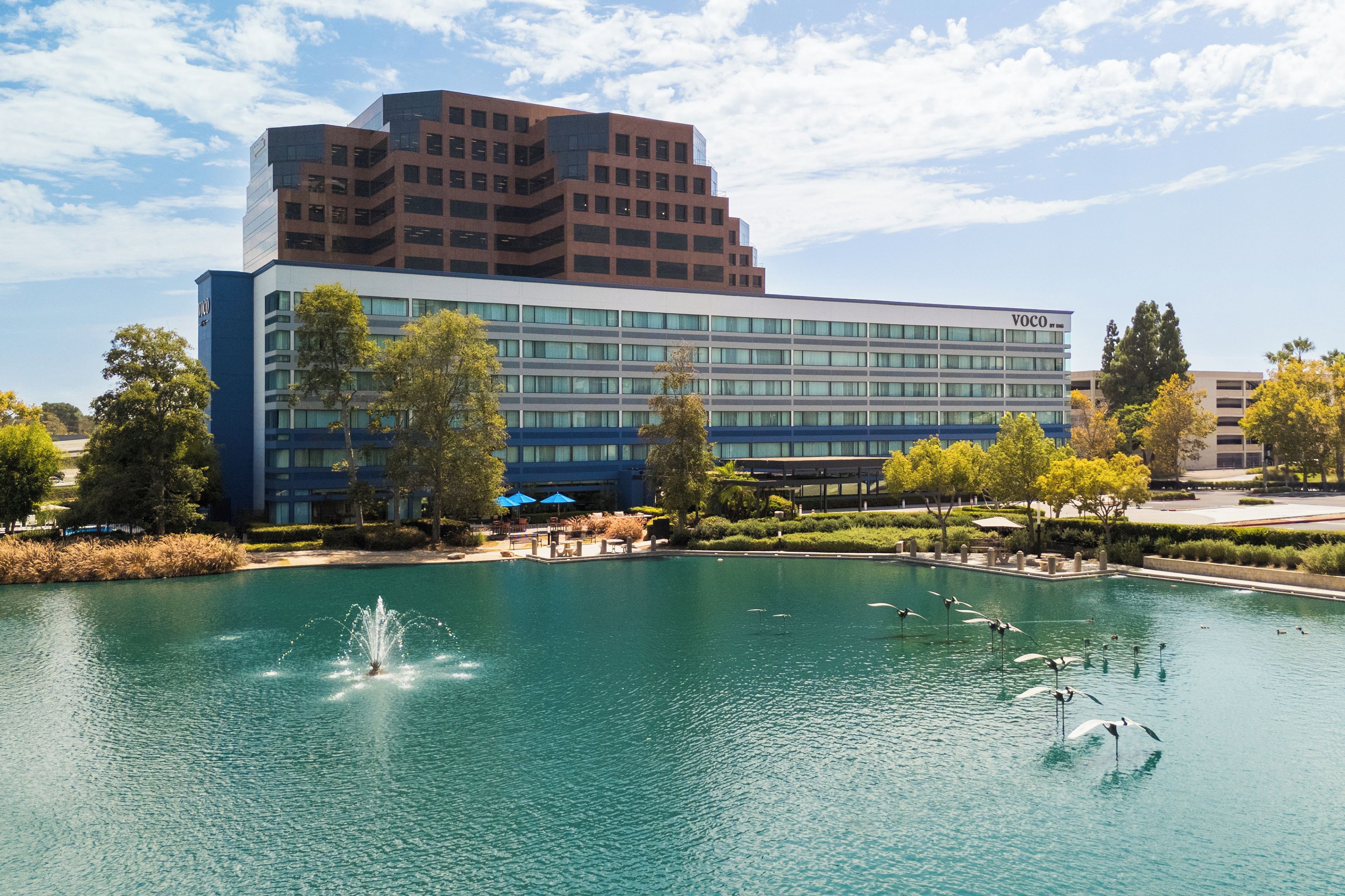 A hotel with a large pool, a fountain, and a modern building with multiple floors.