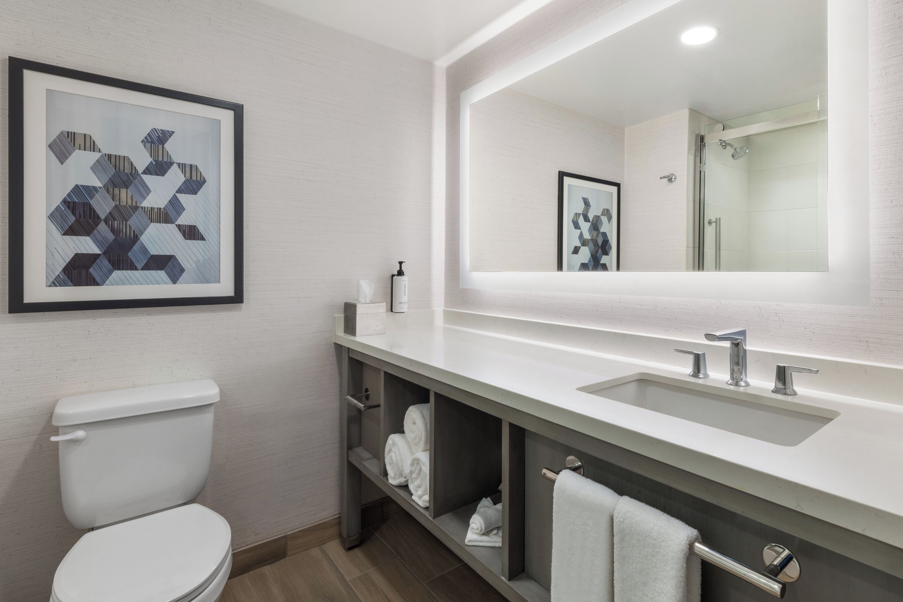 Un baño moderno con inodoro, lavamanos, espejo y ducha. Hay toallas y artículos de aseo en la encimera.