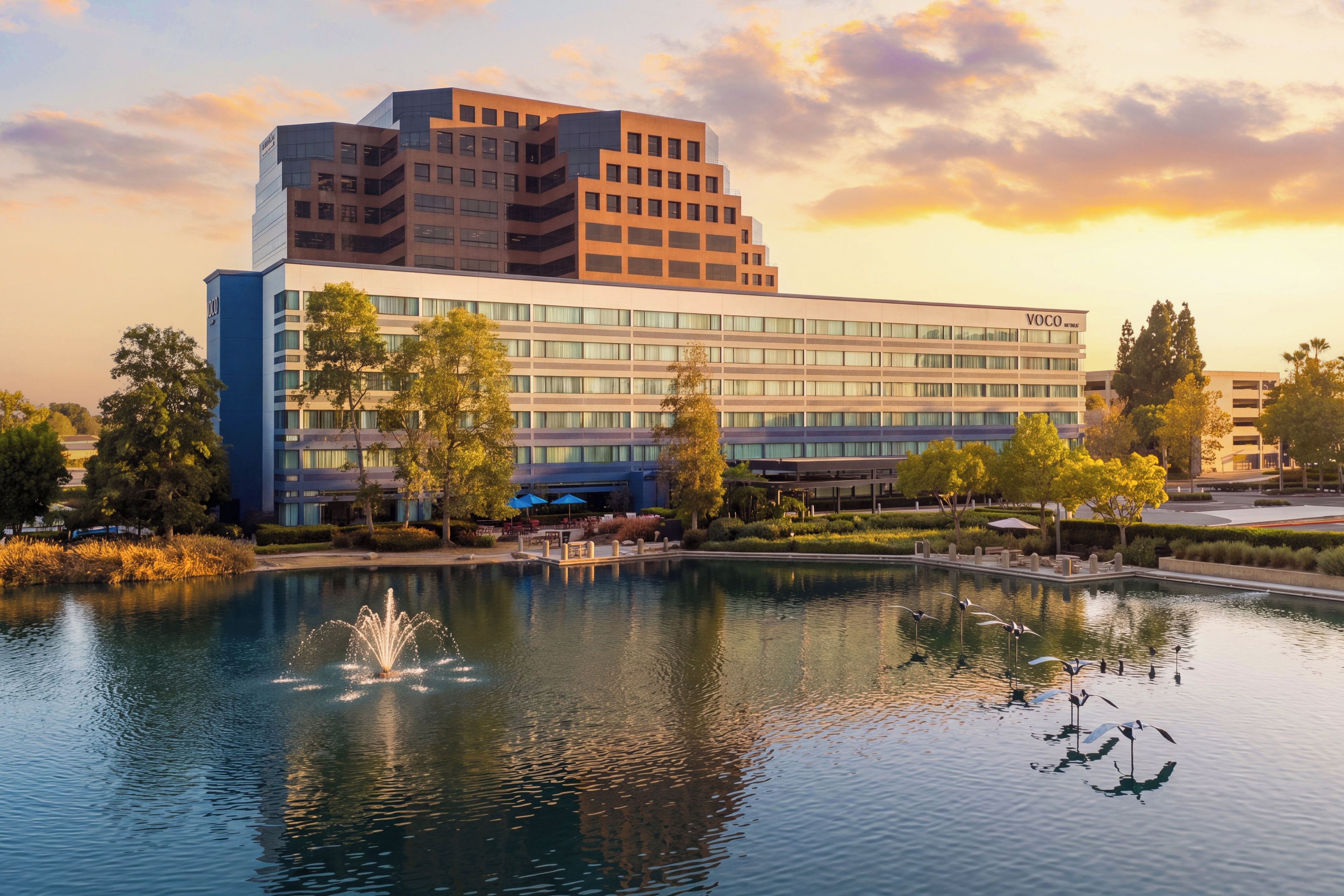 A modern hotel with a large building, a reflecting pool, and a fountain.