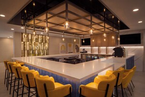 Una cocina moderna con una isla central, taburetes de bar, iluminación colgante y un televisor de pantalla plana grande.