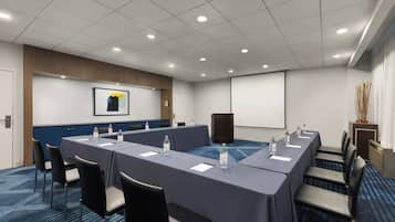 Une salle de conférence équipée d’une longue table, de chaises, d’un écran de projection et d’un système audio.