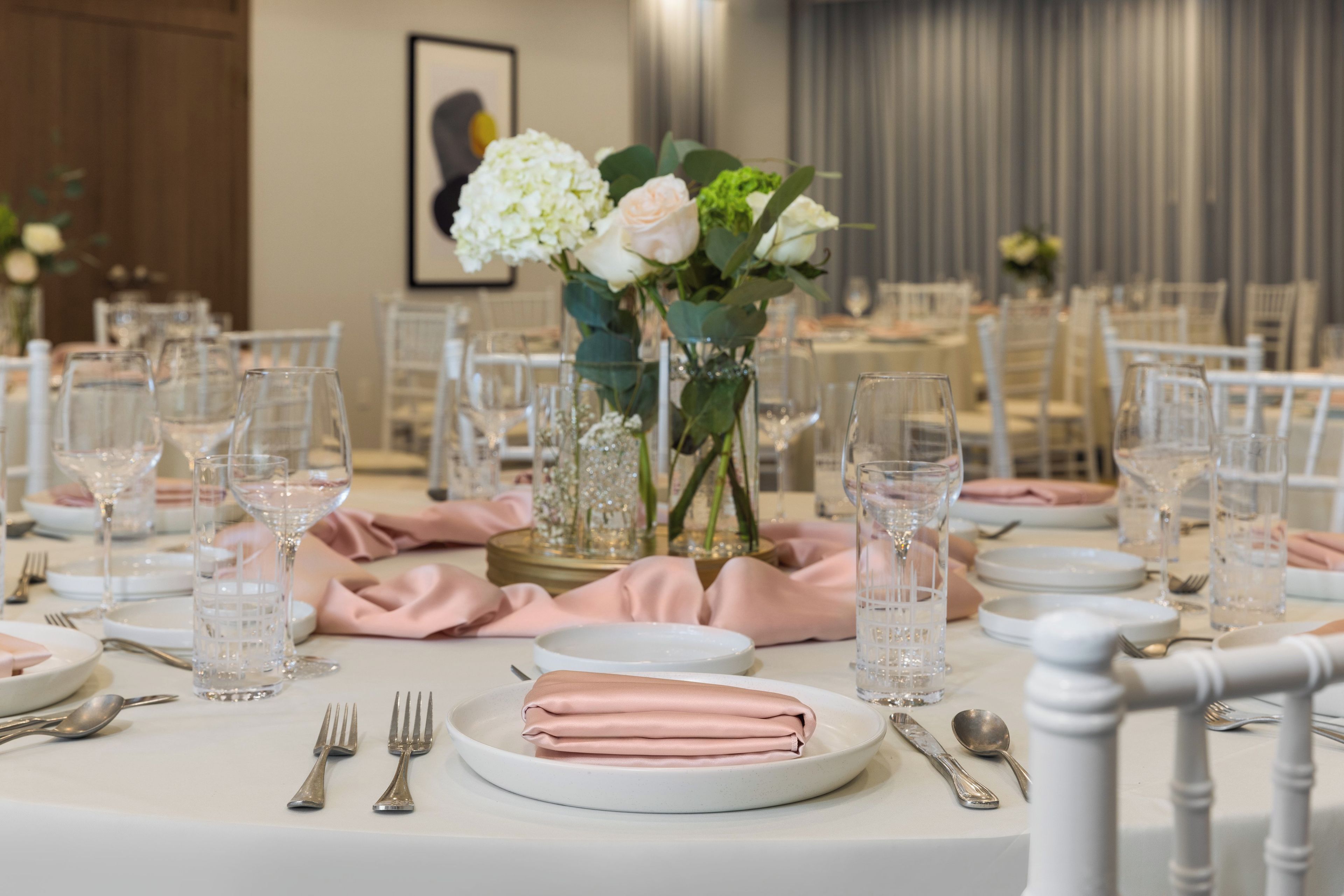 A dining table set with plates, cutlery, and glasses, with a vase of flowers in the center.