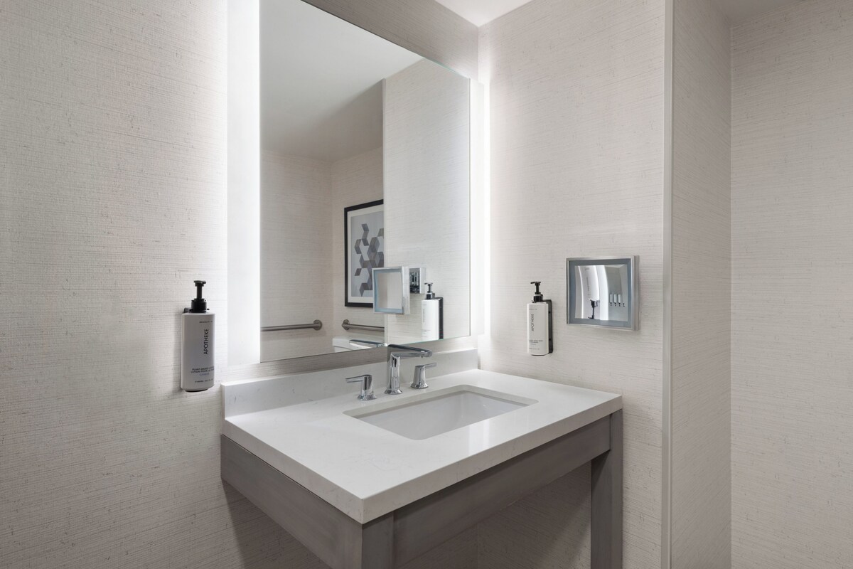A modern bathroom with a large mirror, two sinks, and a shower.