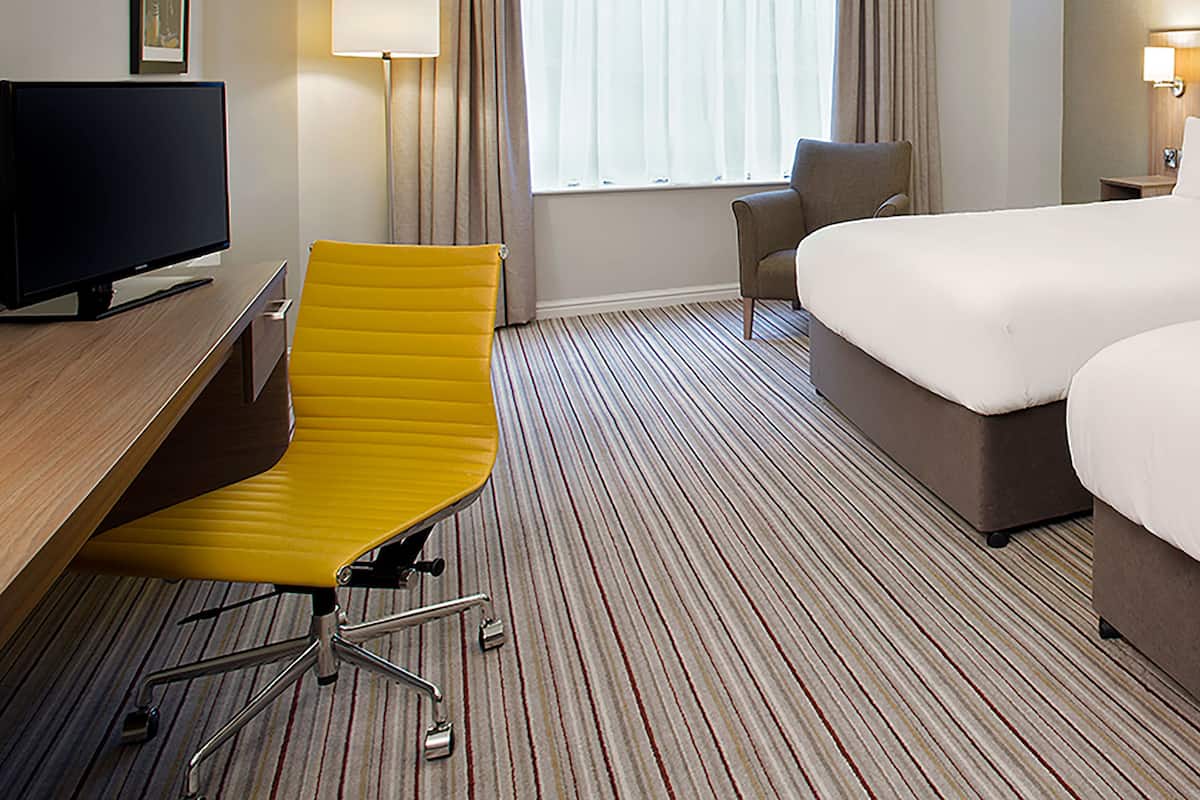 Ein Hotelzimmer mit einem Bett, einem Schreibtisch mit Stuhl, einem Fernseher und einem Fenster mit Vorhängen.