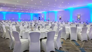 A banquet hall with round tables, white chairs, and blue lighting.