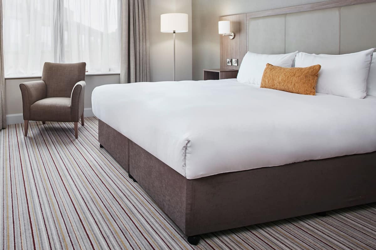 Ein Hotelzimmer mit einem großen Bett, einem Sessel, einem Nachttisch und einer Lampe.