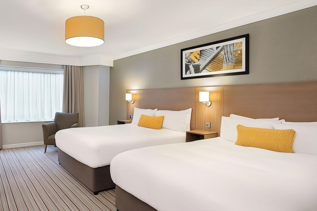 Una habitación de hotel con dos camas, una silla, una lámpara y un cuadro en la pared.