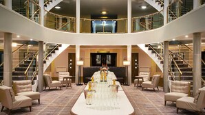 A spacious lobby with a central table set for a banquet, flanked by seating areas and a grand staircase. - Leonardo Hotel and Conference Venue Hinckley Island (Hinckley)
