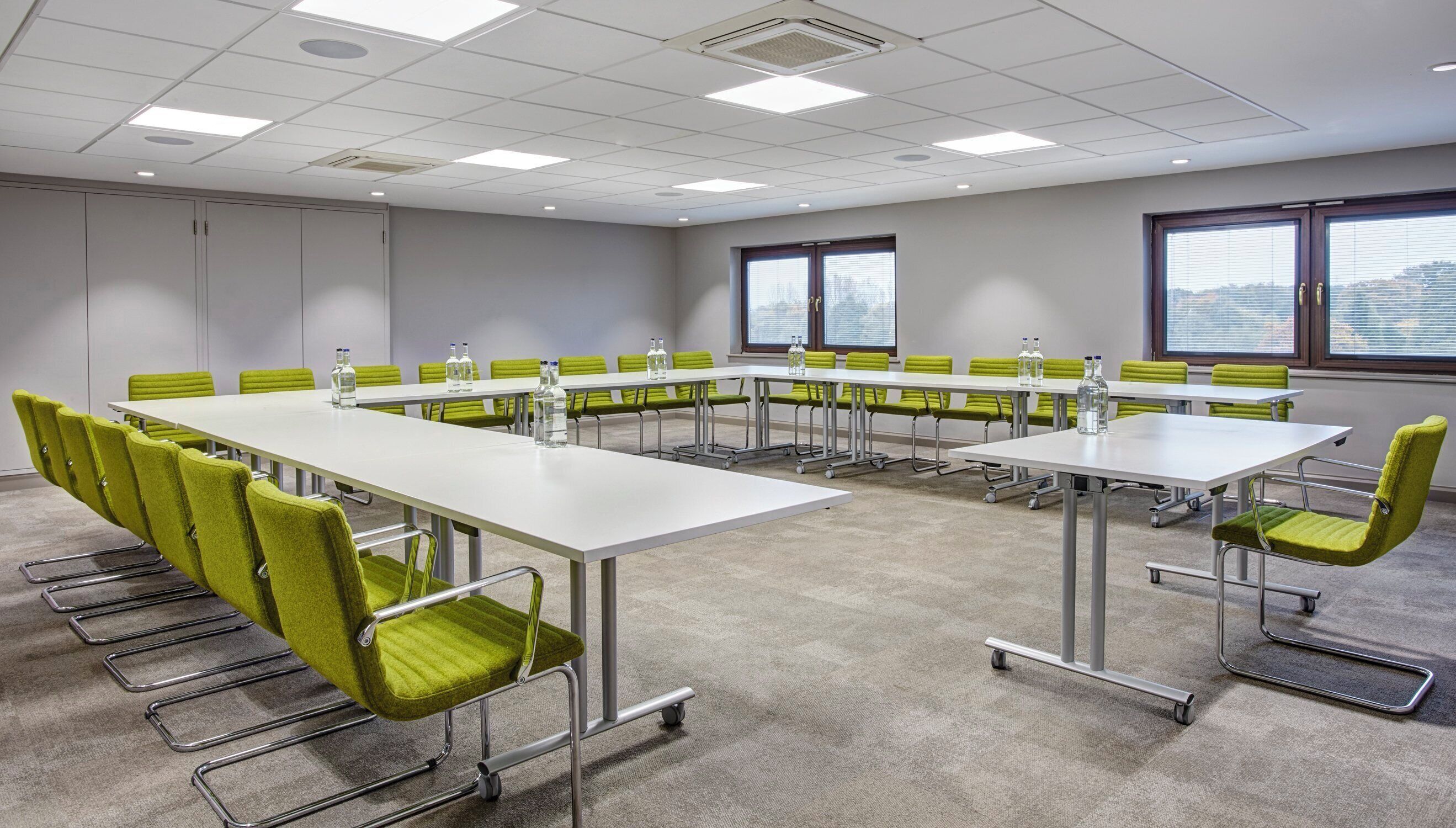A conference room with a long table, green chairs, and large windows.