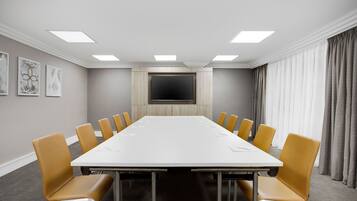 A conference room with a long table, yellow chairs, a flat-screen TV, and a large window with curtains.