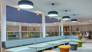 A modern lounge area with a light blue sofa, round tables, and colorful stools. - Leonardo Hotel and Conference Venue Hinckley Island (Hinckley)