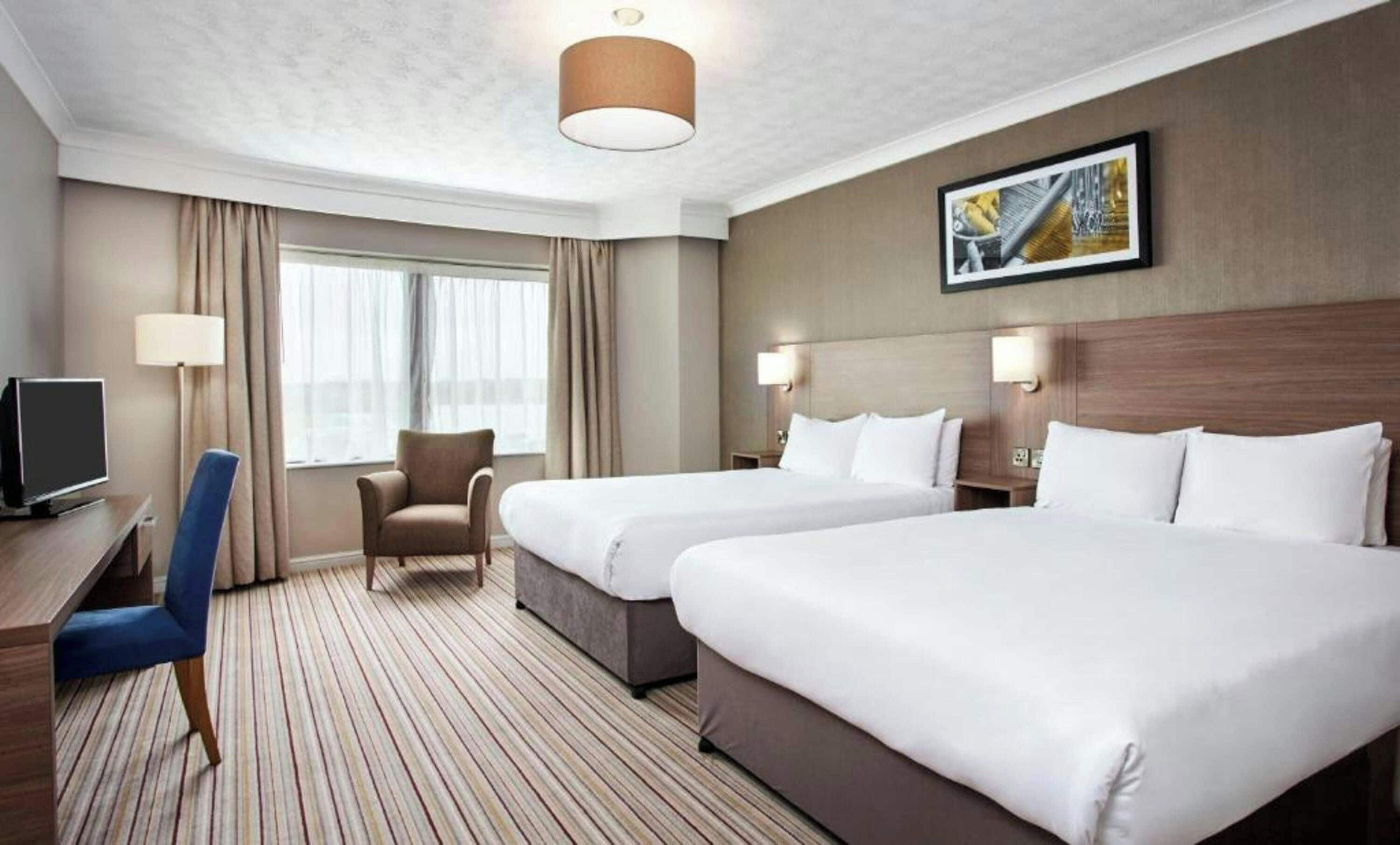 Une chambre d’hôtel avec deux lits, un bureau, une chaise et un téléviseur.