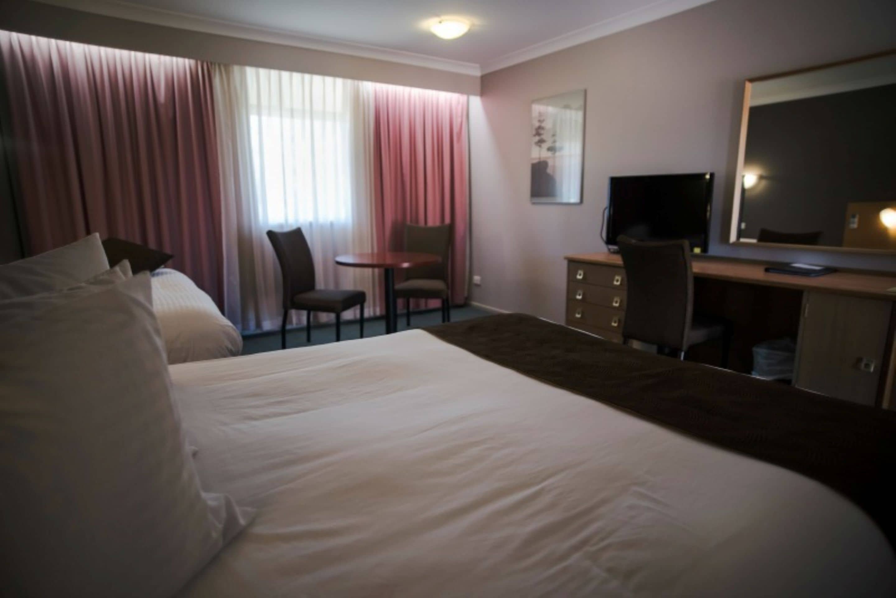 A hotel room with a large bed, a desk with a computer, a chair, and a television.