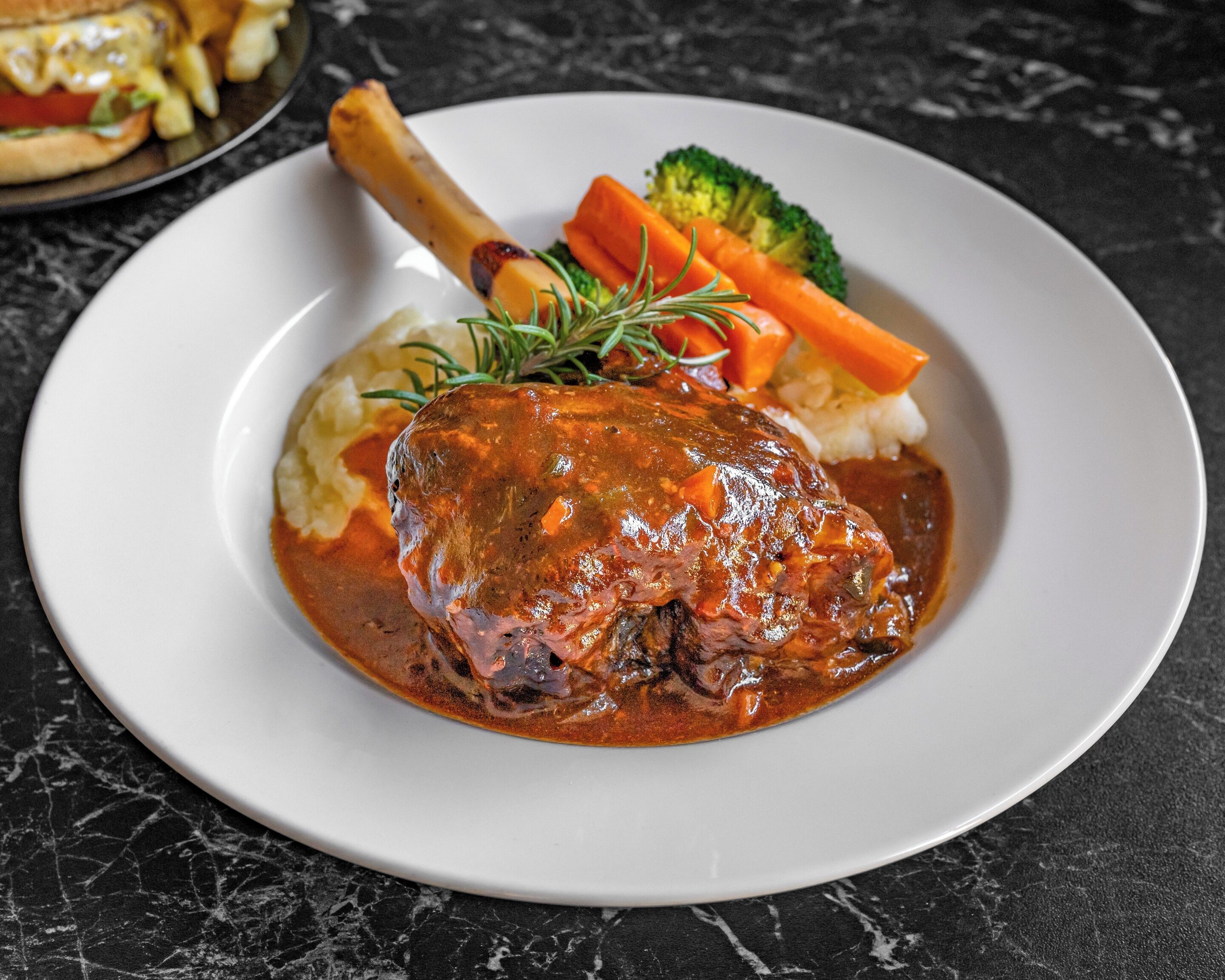 A plate of food with a roasted meat, mashed potatoes, carrots, and broccoli.