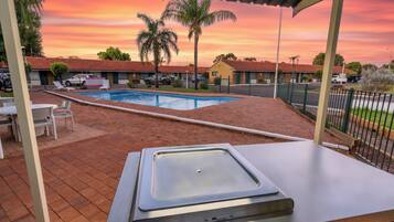 Zona de piscina con área de descanso cubierta, piscina y vistas al atardecer.