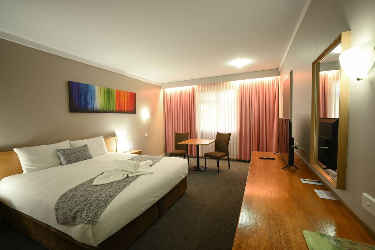 Ein Hotelzimmer mit Bett, Nachttisch, Lampe, Stuhl, Tisch und einem großen Spiegel.