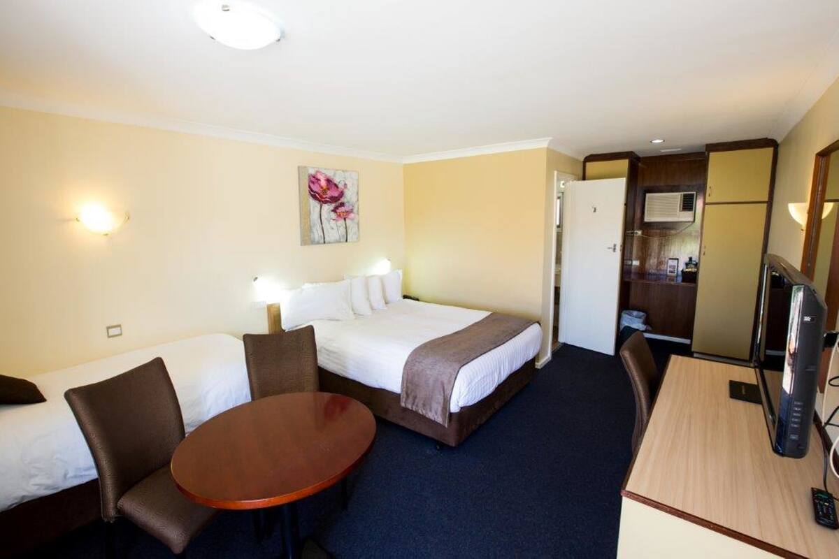 Ein Hotelzimmer mit zwei Betten, einem Schreibtisch, einem Sessel, einem Fernseher und einem Bild an der Wand.