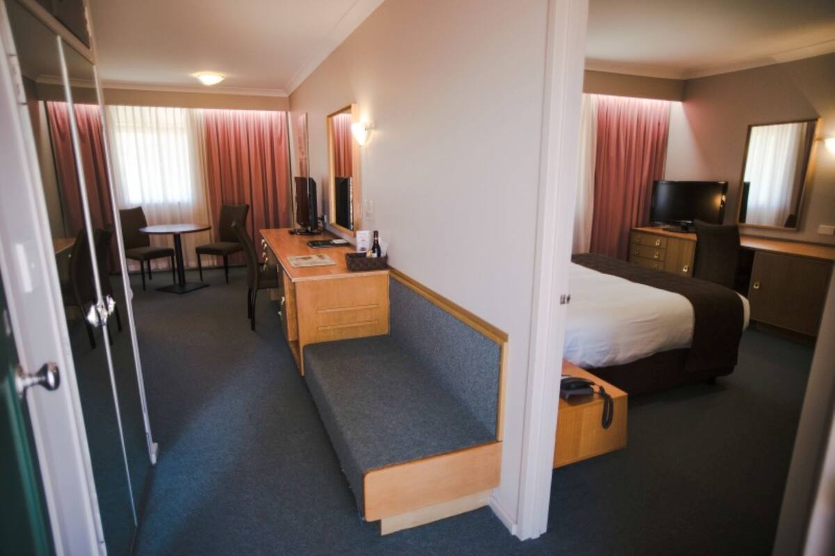 Ein Hotelzimmer mit Bett, Schreibtisch, Stuhl, Fernseher und Kleiderschrank.