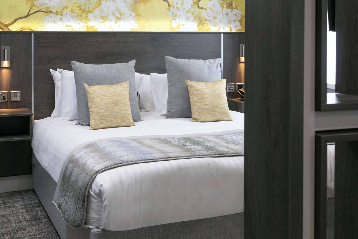 A modern bedroom with a large bed, grey and white bedding, and a decorative wall with floral patterns.