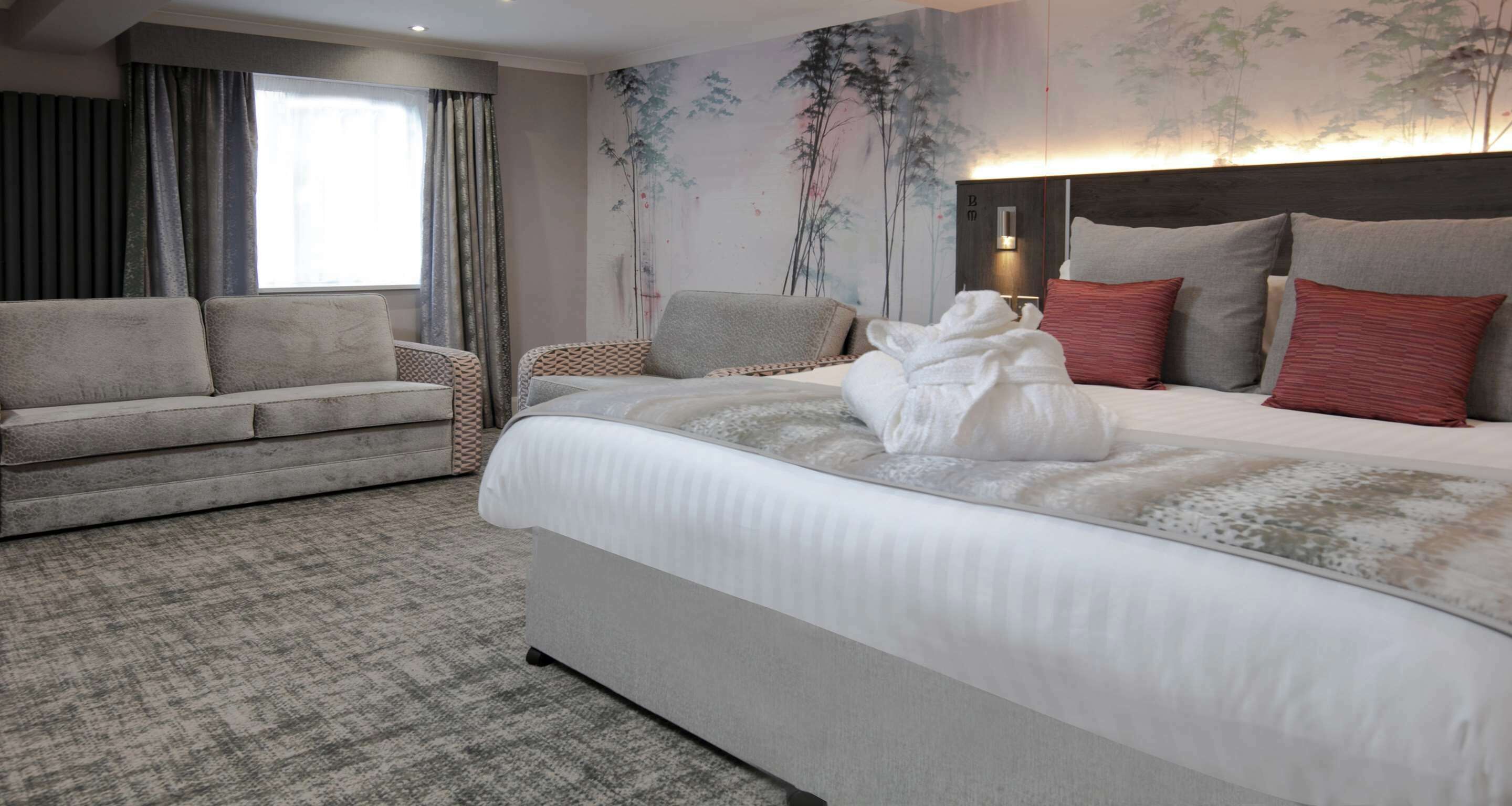 A hotel room with a bed, a sofa, a wall with a painting, and a window with curtains.